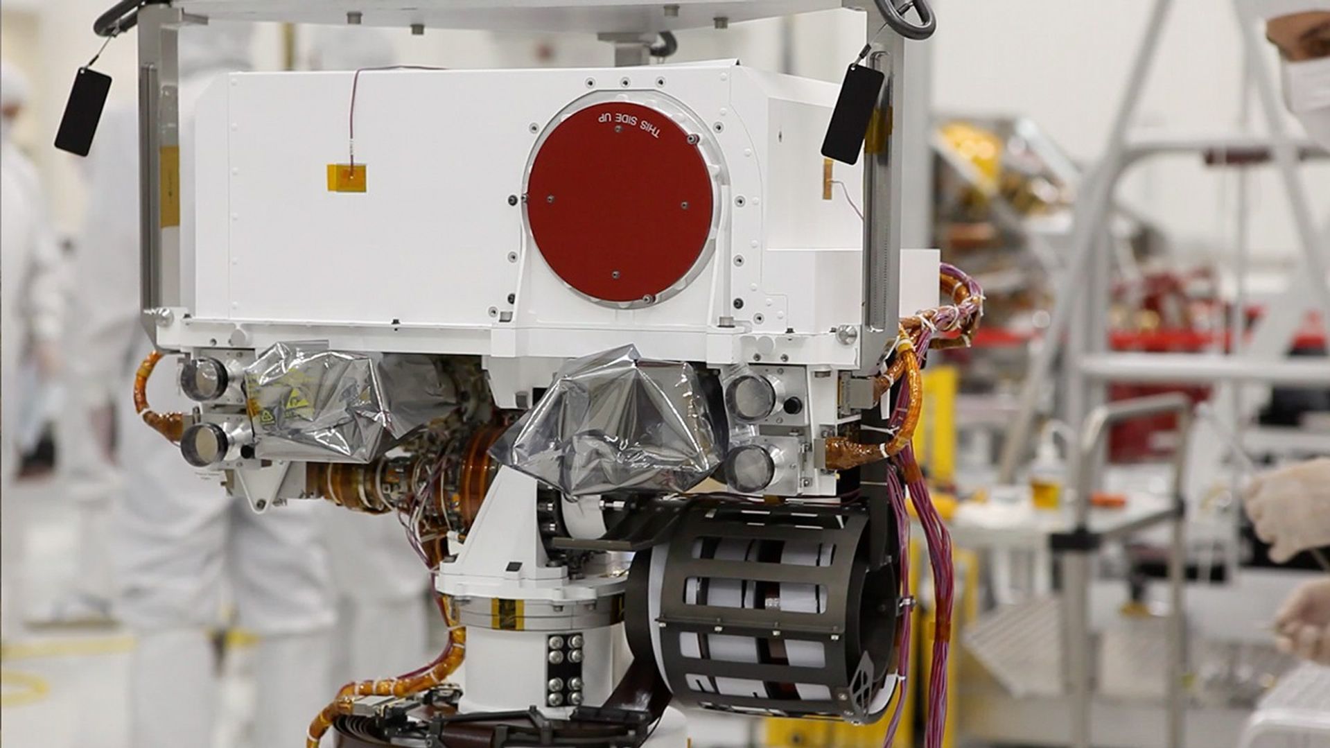 This image shows a close-up of the rover's "head." At the top is a white box structure with a large red circle (the rover's laser called ChemCam) to the right. Beneath the box are two cameras, which will provide views of the Martian surface. They are covered with protective silvery material.