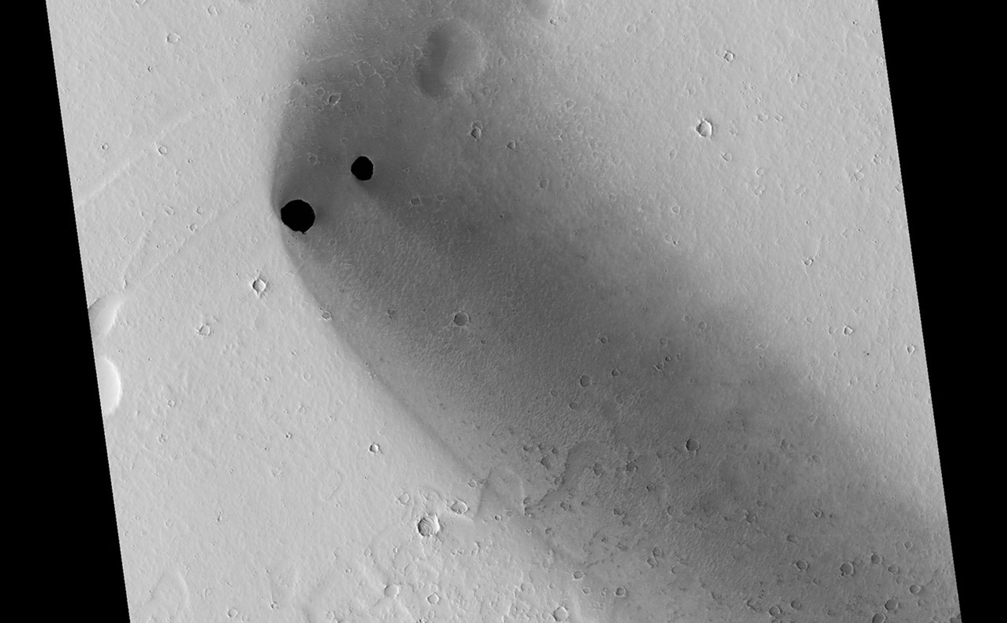 Two dark, rimless pits are located to the northwest of Ascraeus Mons in the Tharsis volcanic region of Mars.