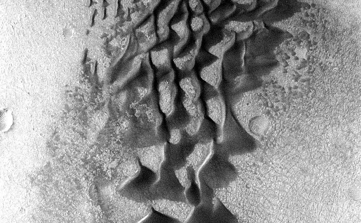 Fans and ribbons of dark sand dunes creep across the floor of Bunge Crater in response to winds blowing from the direction at the top of the picture.