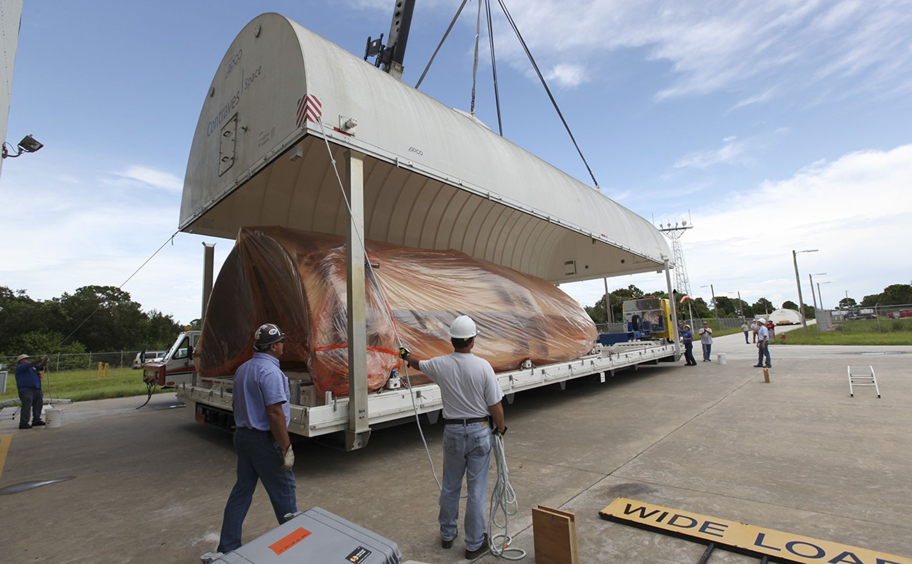 At the Payload Hazardous Servicing Facility at NASA's Kennedy Space Center in Florida, workers uncover half of the Atlas V payload fairing for NASA's Mars Science Laboratory (MSL) mission, encased in plastic, on its transportation pallet.