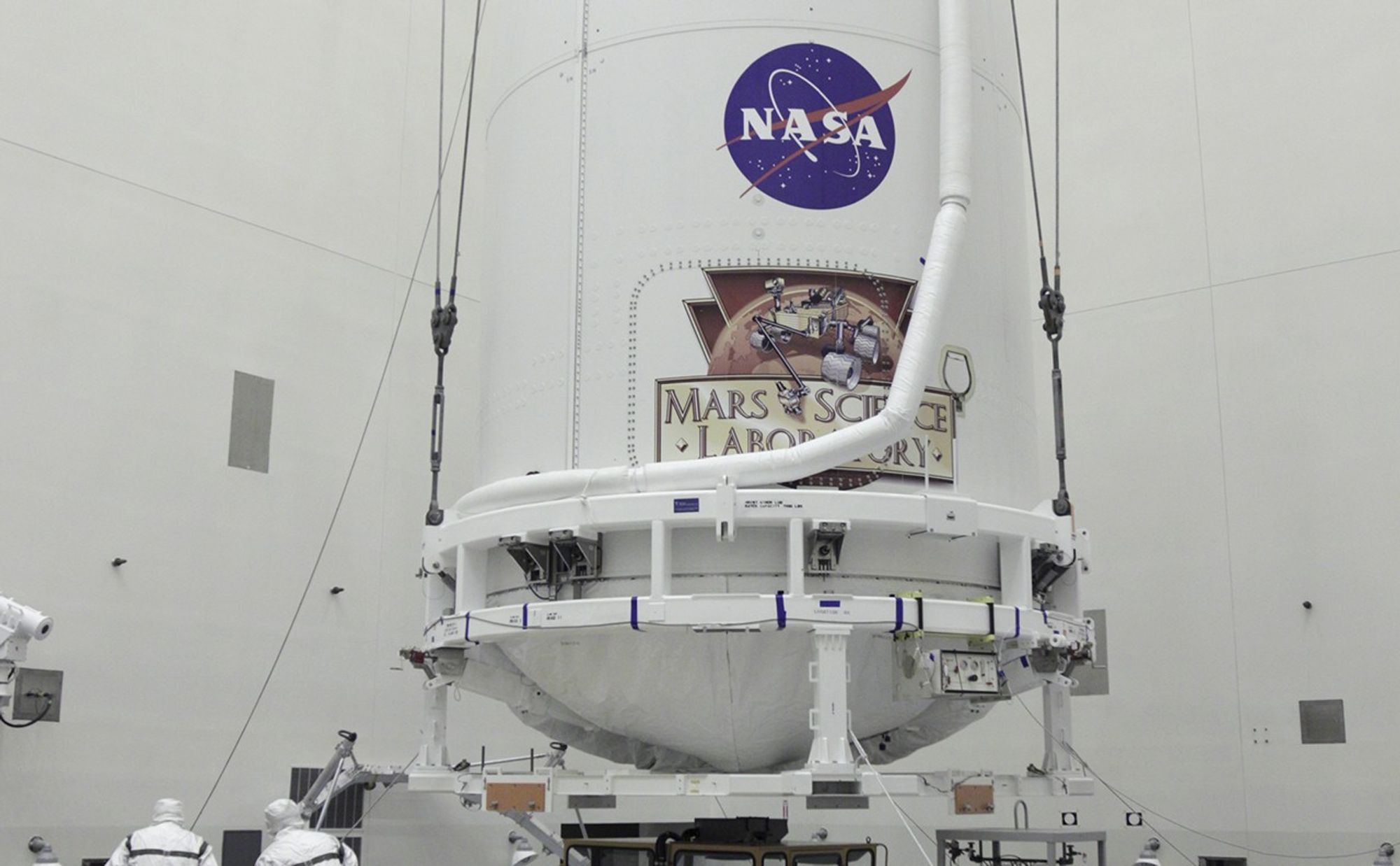 In the Payload Hazardous Servicing Facility at NASA's Kennedy Space Center in Florida, technicians assist as the payload fairing of an Atlas V rocket approaches a transporter for the move to Space Launch Complex 41.