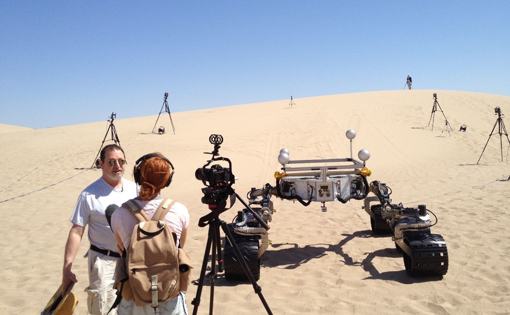 Michael Malin, left, principal investigator for three science cameras on NASA's Curiosity Mars rover, comments to a news reporter during tests with Curiosity's mobility-test stand-in, Scarecrow, on Dumont Dunes in California's Mojave Desert.