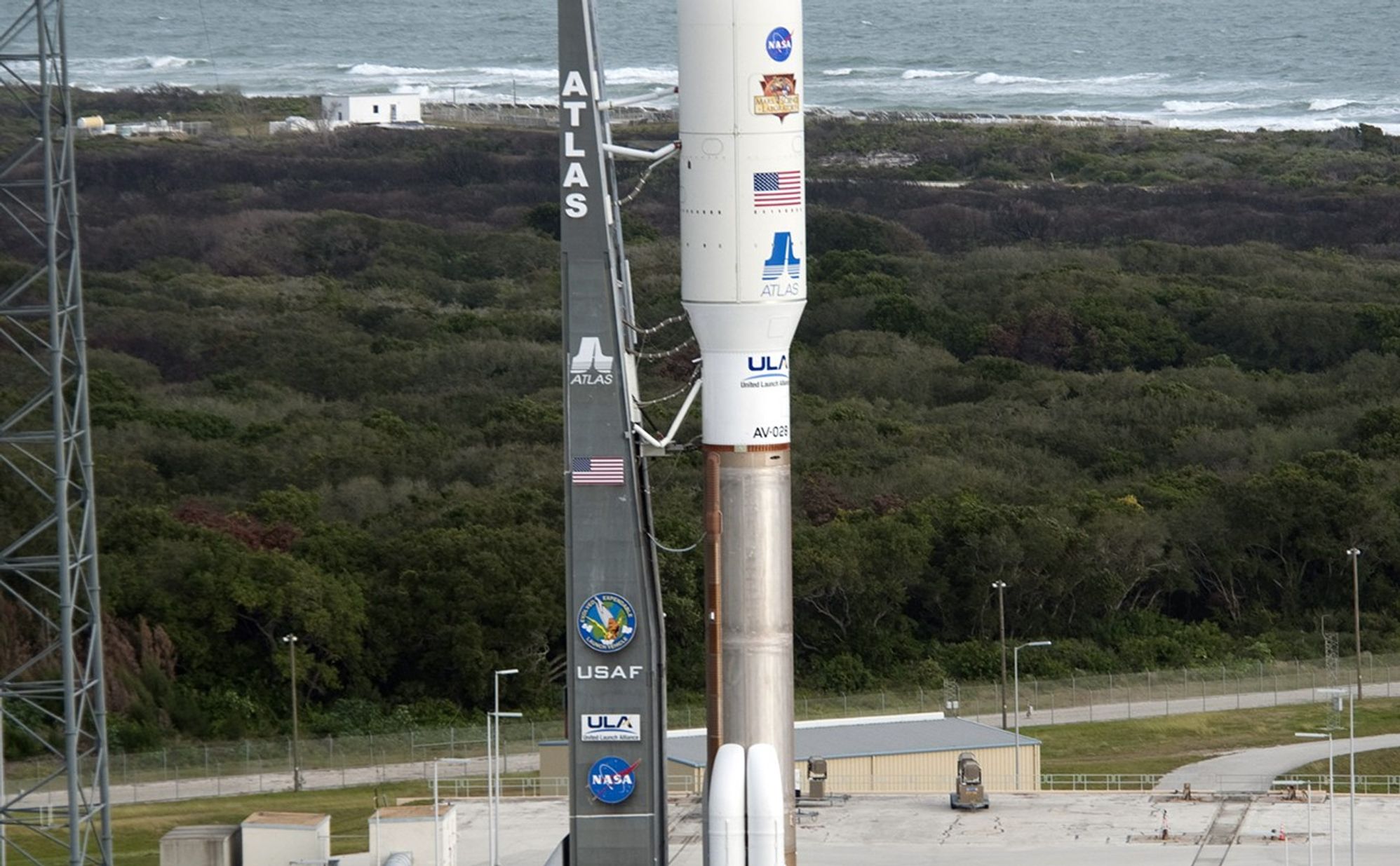 On Cape Canaveral Air Force Station in Florida, the 197-foot-tall United Launch Alliance Atlas V rocket arrives on the launch pad at Space Launch Complex-41, situated near the Atlantic Ocean.