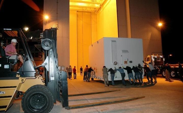 Workers roll one of two containers with the Mars Reconnaissance Orbiter equipment into the Payload Hazardous Servicing Facility, Kennedy Space Center.