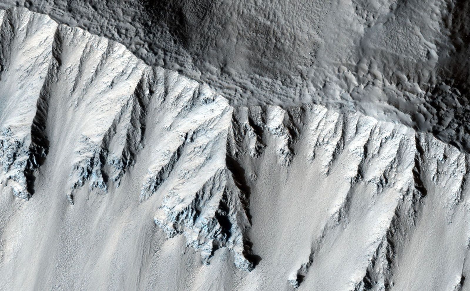 This fresh crater is located in the northern mid-latitudes. It is designated as fresh because of its very sharp rim.The crater has experienced some modification since it formed, including a few tiny craters on the south wall.The rough texture of the floor is suggestive of ground ice, which is expected to exist in the mid-latitudes. Ground ice aids gravity in moving material from the crater walls towards the center. Material is visible slumping off the northwest crater wall in this fashion. The wavy texture of the center of the crater floor suggests that material has been transported from the walls and merged in the center.