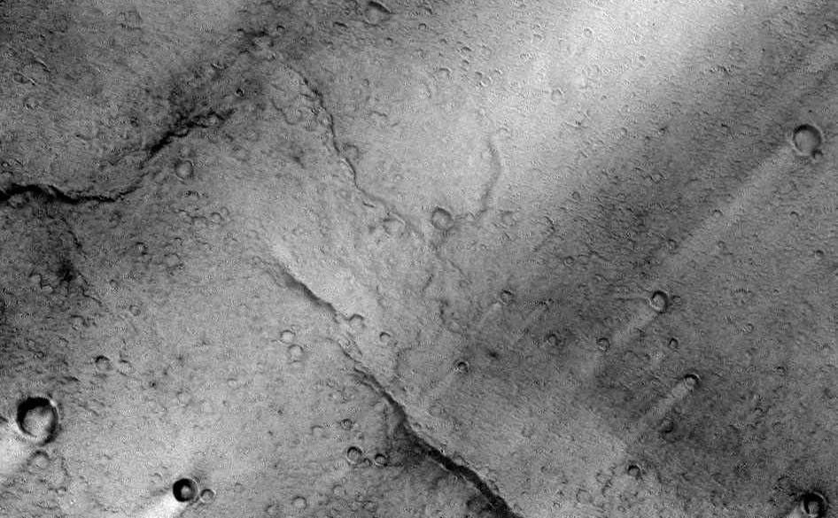 This image is near the southern edge of a low, broad volcanic feature called Syrtis Major. A close look at this image reveals a wrinkly texture that indicates a very rough surface that is associated with the lava flows that cover this region. On a larger scale, there are numerous bright streaks that trail topographic features such as craters. These bright streaks are in the wind shadows of the craters where dust that settles onto the surface is not as easily scoured away. It is important to note that these streaks are only bright in a relative sense to the surrounding image. Syrtis Major is one of the darkest regions on Mars and it is as dark as fresh basalt flows or dunes are on Earth.