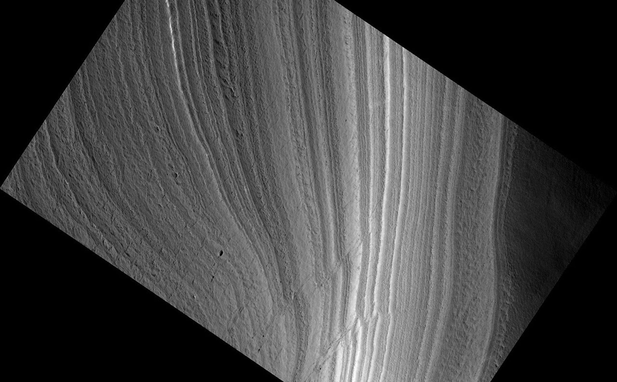 This image shows an outcrop of the south polar layered deposits (SPLD). The SPLD consist of layers of ice and admixed dust and make up the bulk of the dome-shaped Planum Australe.Planum Australe is, in some ways, analogous to the Antarctic ice sheet. Troughs and scarps carved into Planum Australe by erosional processes have exposed SPLD layers within it. In this image, the darkest area at the bottom of the image is the bottom of the scarp. Except for the dark material at the bottom of the slope, much of the changes in brightness in this image are due to the lighting angle, the direction from which the sun is illuminating the slope.Much like ice cores from Greenland and Antarctica and deep sea sediment cores, the icy-dusty layers of the SPLD may have preserved a record of recent Mars climate history. Understanding that record is a complex process and involves, among many other types of analyses, examining the differences and similarities in appearance between each layer and attempting to classify layer types. This image shows nice examples of different layer textures. But what is especially interesting about this image are the faults cutting through the layers. These faults appear as diagonal lines, on either side of which, the layering is offset. Note that the faults are not clean, single lines, but appear in long groups of short lines.What caused these faults is still under investigation, but, among other possibilities, they could be related to an earlier time when temperatures were higher and the ice was flowing at a much faster rate than it is today.