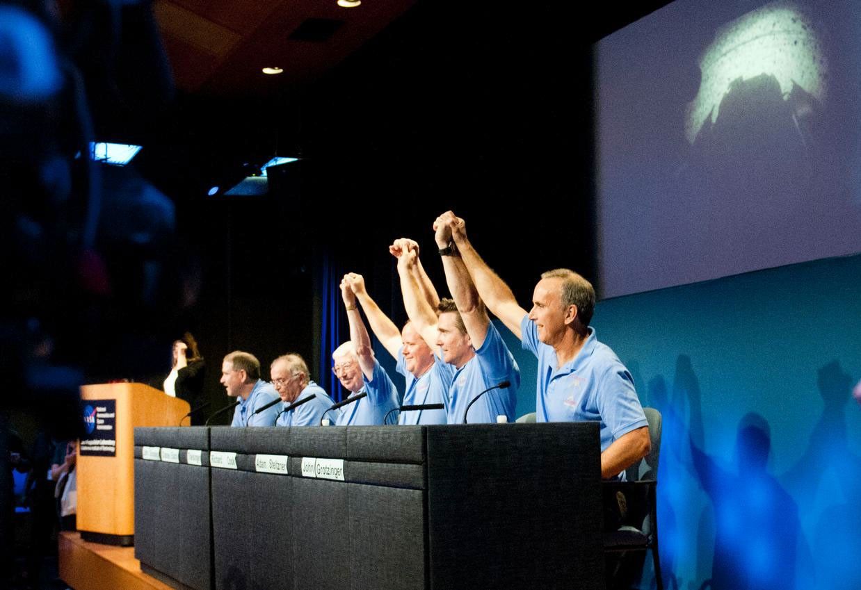 Mars Science Laboratory mission scientists, flight controllers, managers and administrators raise their hands to a cheering crowd at a news conference following the successful landing of NASA's Curiosity rover on Mars.