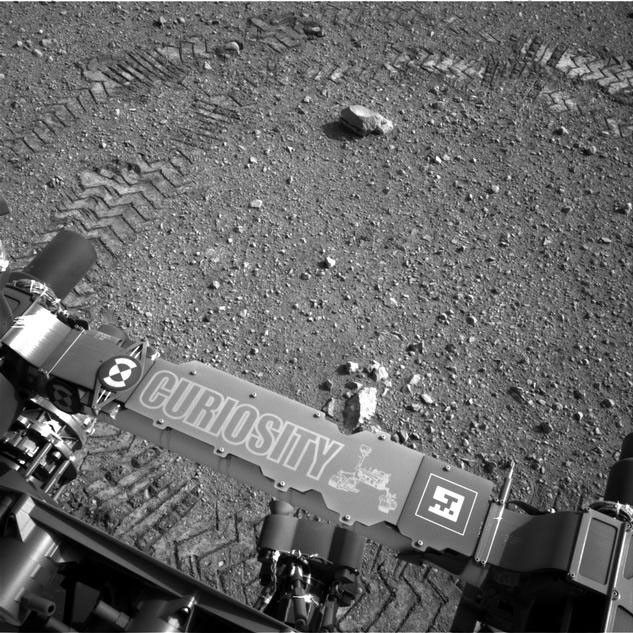 This image shows a close-up of track marks from the first test drive of NASA's Curiosity rover. The rover's arm is visible in the foreground.