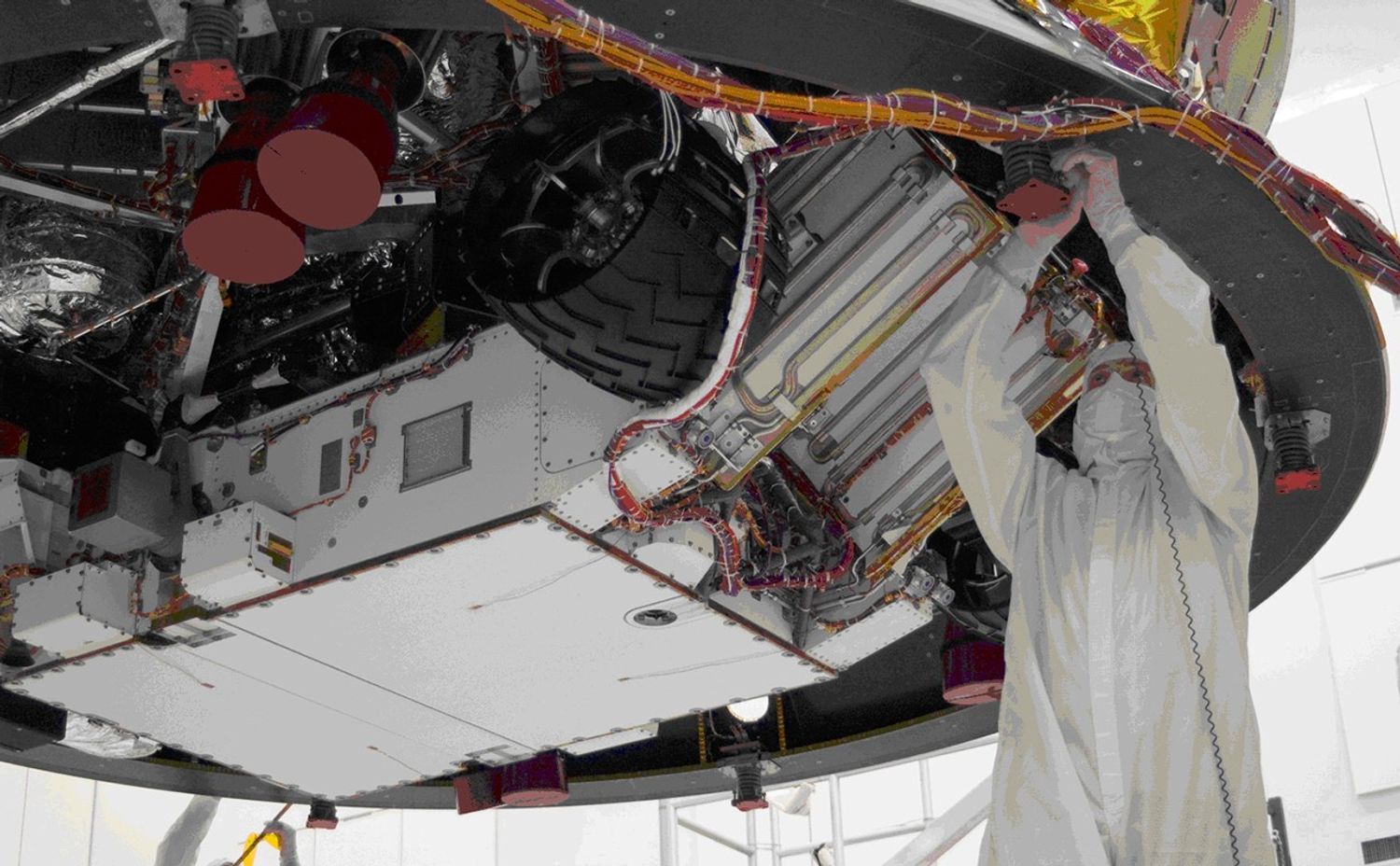 This image shows an engineer dressed in cleanroom coverall working on the rover which is overhead.