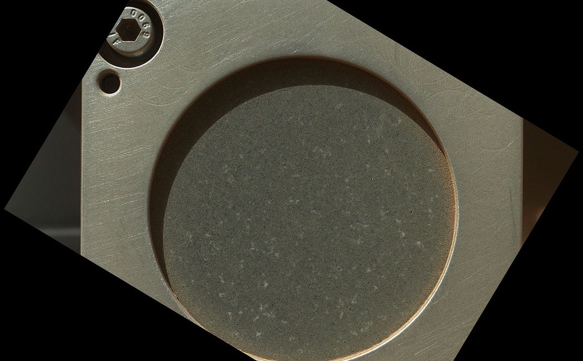 A sample of basaltic rock from a lava flow in New Mexico serves as a calibration target carried on the front of NASA's Mars rover Curiosity for the rover's Canadian-made Alpha Particle X-Ray Spectrometer (APXS) instrument.