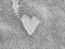 The Mars Global Surveyor (MGS) Mars Orbiter Camera (MOC) captured this unique view of a bright, heart-shaped mesa in the south polar region on November 26, 1999. The presence of this mesa indicates that the darker, rough terrain that surrounds it was once covered by a layer of the bright material.