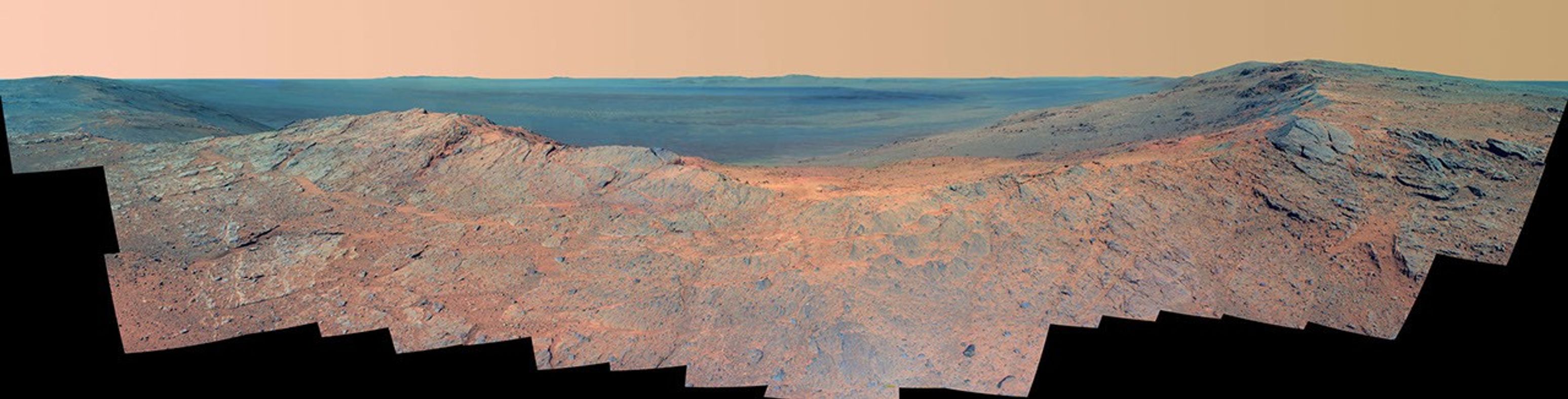 This May 14, 2014, scene from the Pancam on NASA's Mars Exploration Rover Opportunity catches "Pillinger Point," on the western rim of Endeavour Crater, in the foreground and the crater's eastern rim on the horizon. The scene's false color makes differences in surface materials more easily visible.