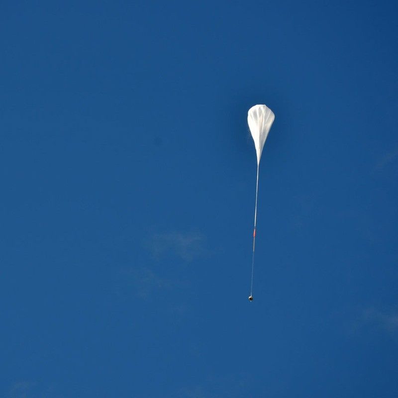 The test vehicle rides on a long, while balloon, against a clear blue sky.