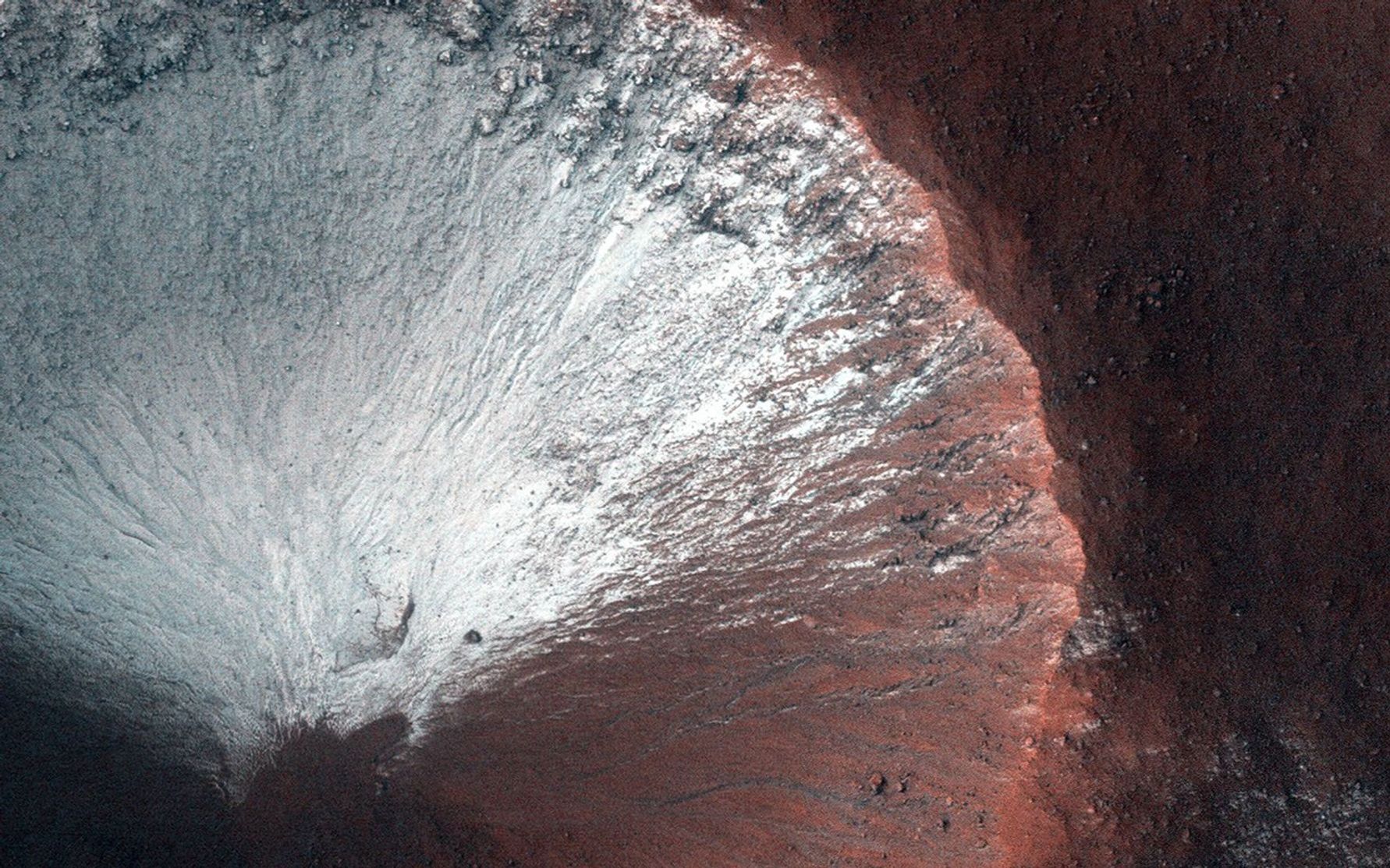 This image shows frost on a crater slope. The white frost covers nearly the top side of the crater, while the bottom part appears reddish in color.