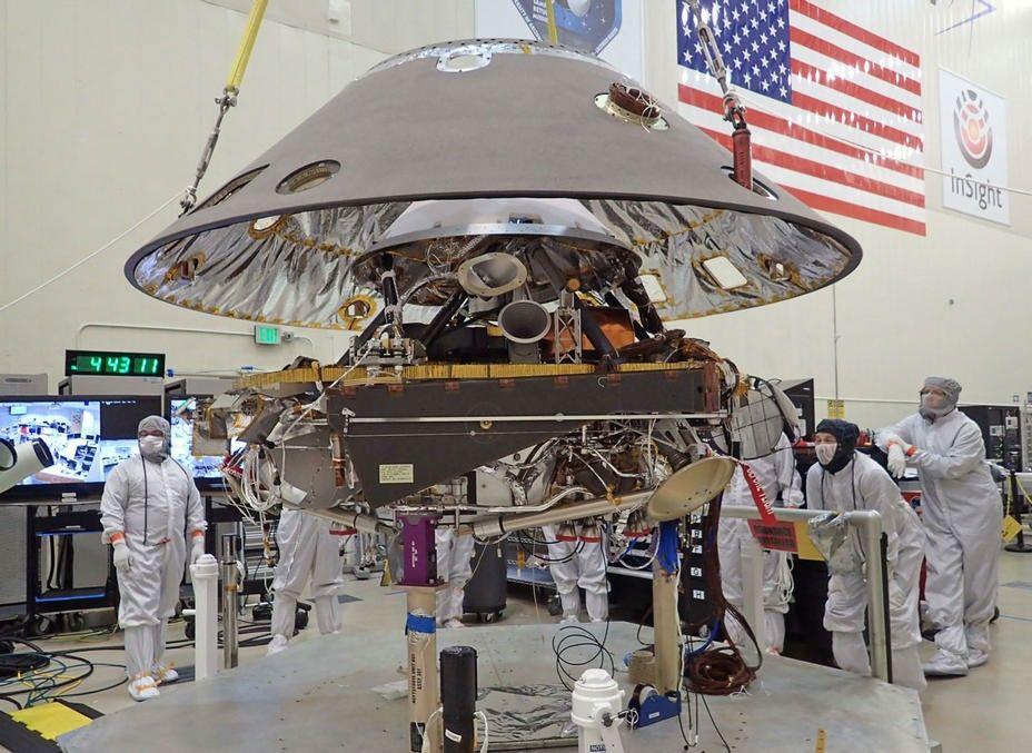 In this photo, the back shell of NASA's InSight spacecraft is being lowered onto the mission's lander, which is folded into its stowed configuration.