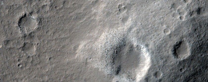 This area of Mars has a few gray craters, with white/light material surrounding it.