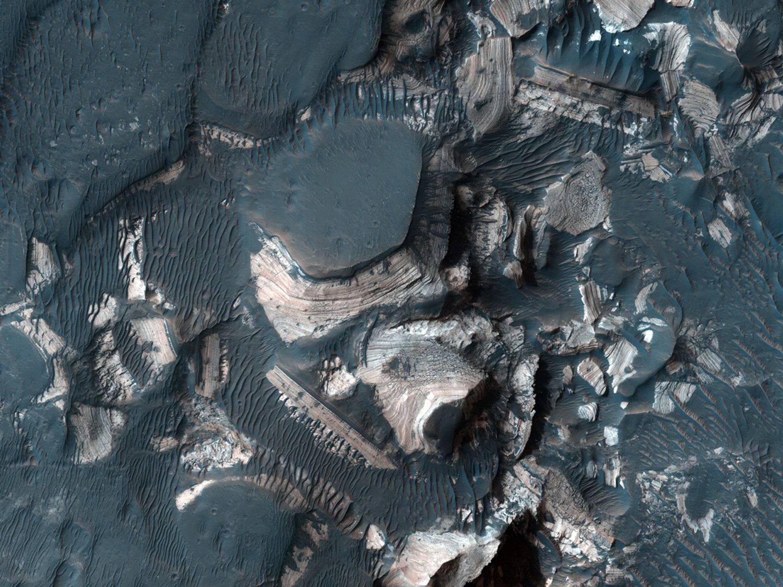 This image shows blocks of bright, layered rock embedded in darker material that are thought to have been deposited by a giant flood that occurred when Uzboi Valles breached the rim of Holden Crater.