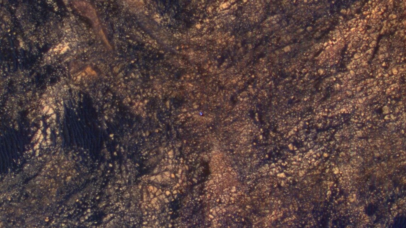 The feature that appears bright blue at the center of this scene is NASA's Curiosity Mars rover on the northwestern flank of Mount Sharp, viewed by NASA's Mars Reconnaissance Orbiter. Curiosity is approximately 10 feet long and 9 feet wide (3.0 meters by 2.8 meters).