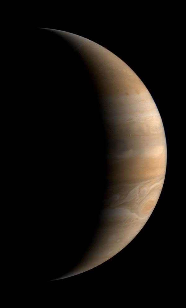 Jupiter has a soft glow with warm shades of brown, tan, and orange in this image from a spacecraft.