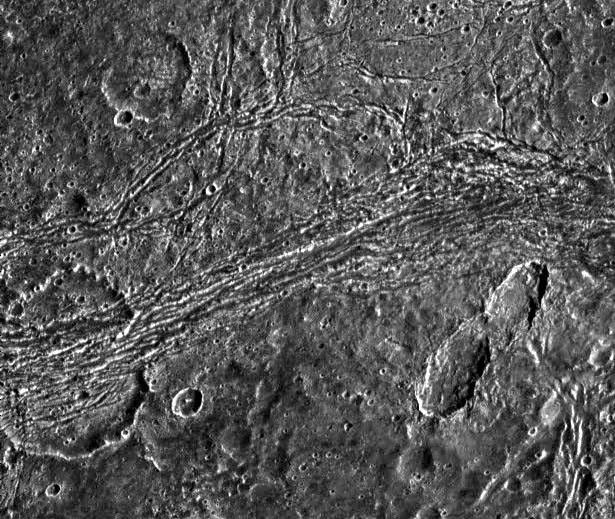 This image captured by NASA's Galileo spacecraft shows dark terrain of Nicholson Regio on Jupiter's moon, Ganymede. On the left is a crater that has been torn apart by tectonic forces.
