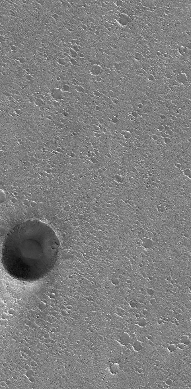 NASA's Mars Global Surveyor shows an impact crater in western Chryse Planitia on Mars surrounded by a flat plain riddled by hundreds of smaller impact craters.