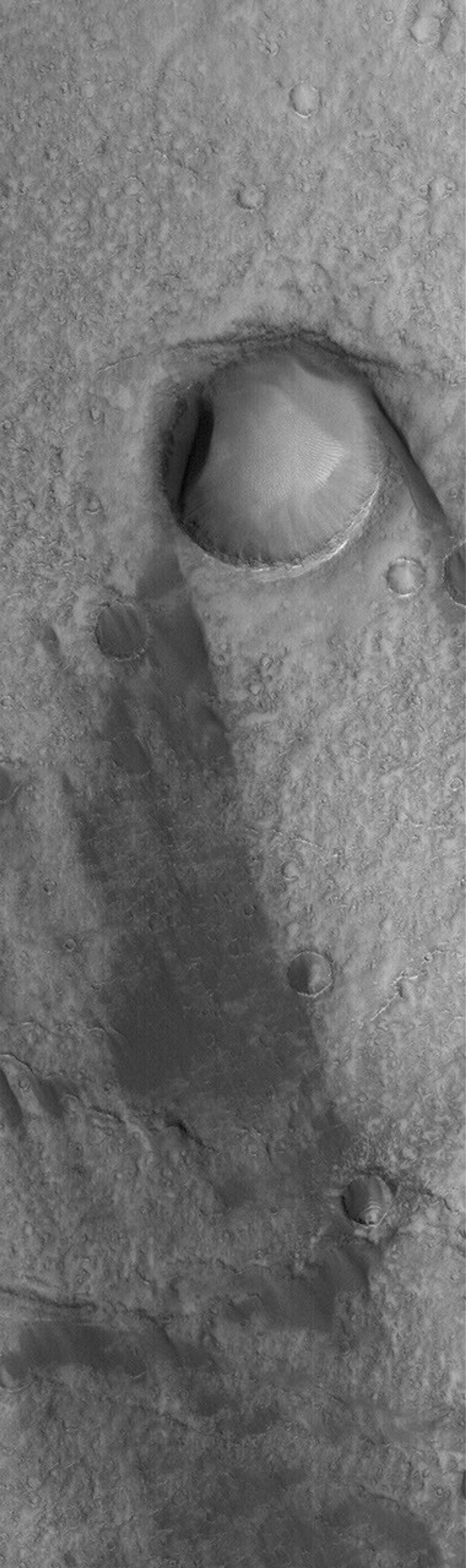 NASA's Mars Global Surveyor shows the results of wind action on the floor of the giant martian impact basin, Huygens. The large crater in this image has a wind streak on its lee side.
