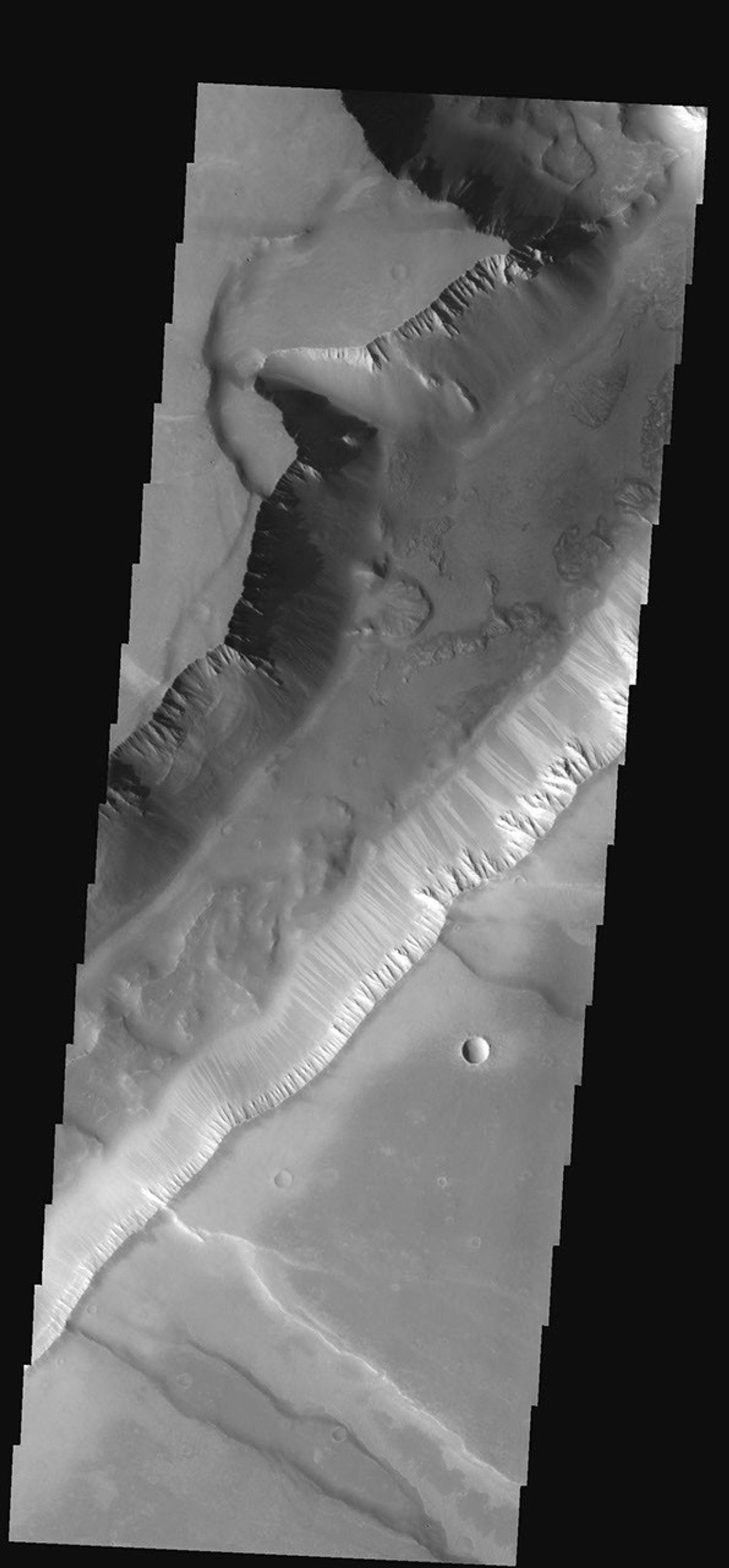This narrow canyon is part of Coprates Chasma on Mars. On the east side of the canyon a landslide is visible. The southern wall of the canyon is marked by bright and dark streaks where dust has slid down the cliff face as seen by NASA's 2001 Mars Odyssey.