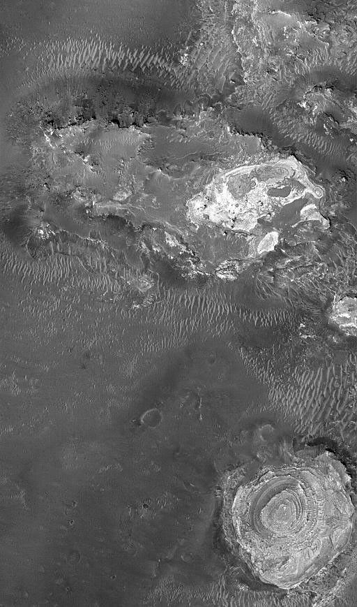 NASA's Mars Global Surveyor shows exposures of light-toned, layered, sedimentary rock among dark-surfaced plains in northern Sinus Meridiani on Mars. A circular feature in the lower right corner is a wedding-cake-like tower of sedimentary rocks.