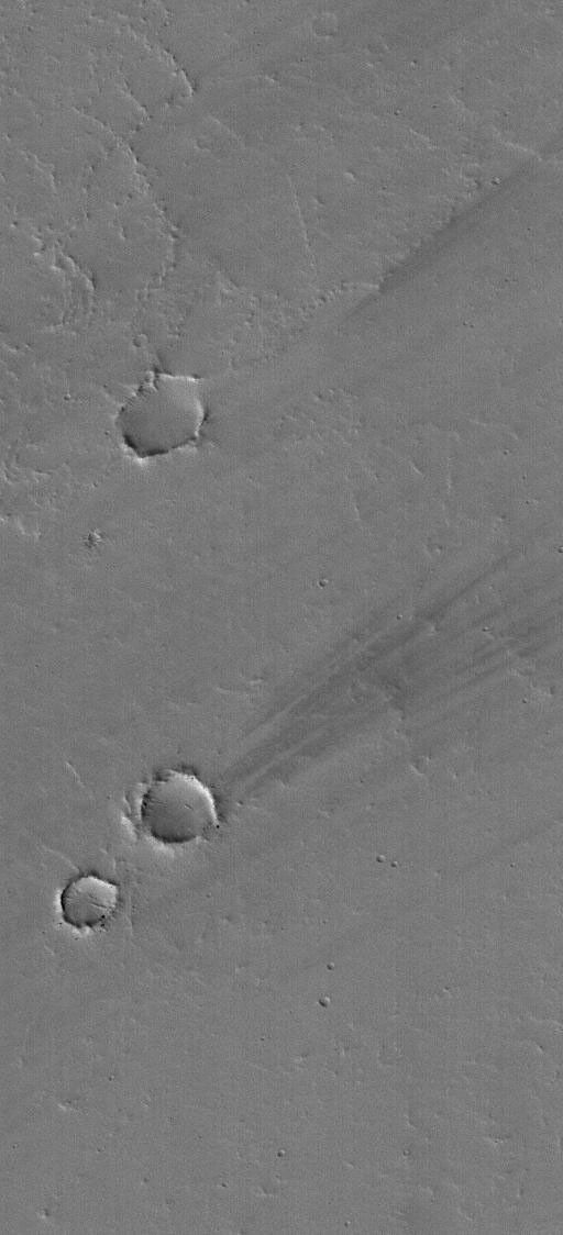 NASA's Mars Global Surveyor shows a few dark wind streaks in the lee, the downwind side, of shallow craters on a lava- and dust-covered plain in eastern Tharsis on Mars.
