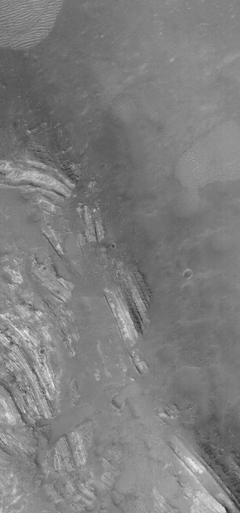 NASA's Mars Global Surveyor shows severely tilted, or dipping, layered rocks in Oudemans Crater in the Valles Marineris region of Mars. The rocks have a light tone and are somewhat broken-up by faults. These rocks were deposited in flat-lying layers.