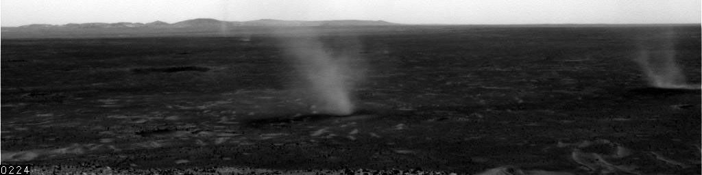 This image shows several dust devils moving from right to left across a plain inside Mars' Gusev Crater, as seen from the vantage point of NASA's Mars Exploration Rover Spirit in hills rising from the plain on July 13, 2005.