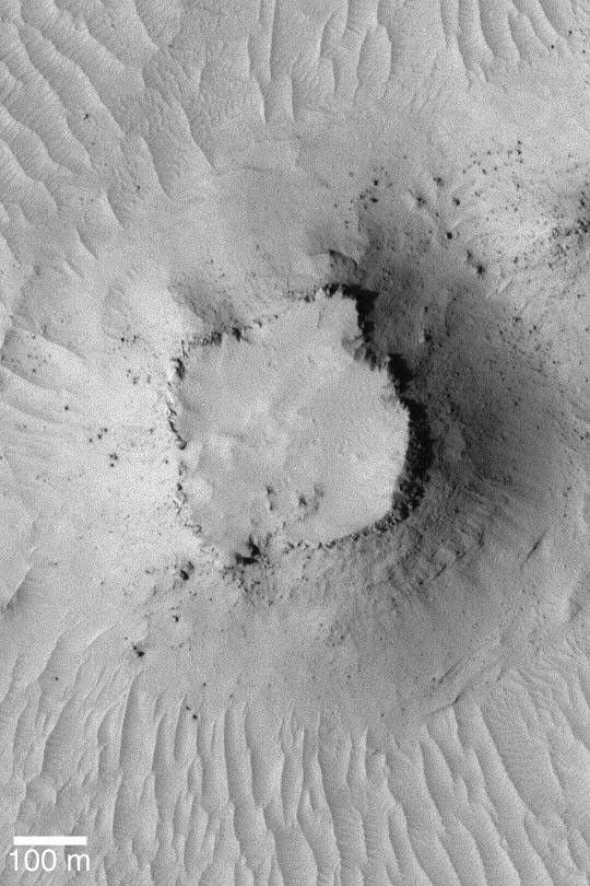 NASA's Mars Global Surveyor shows a small mesa surrounded by a plain of dust-mantled dunes and ripples on Mars. Large, house-sized boulders have tumbled down the mesa slopes.