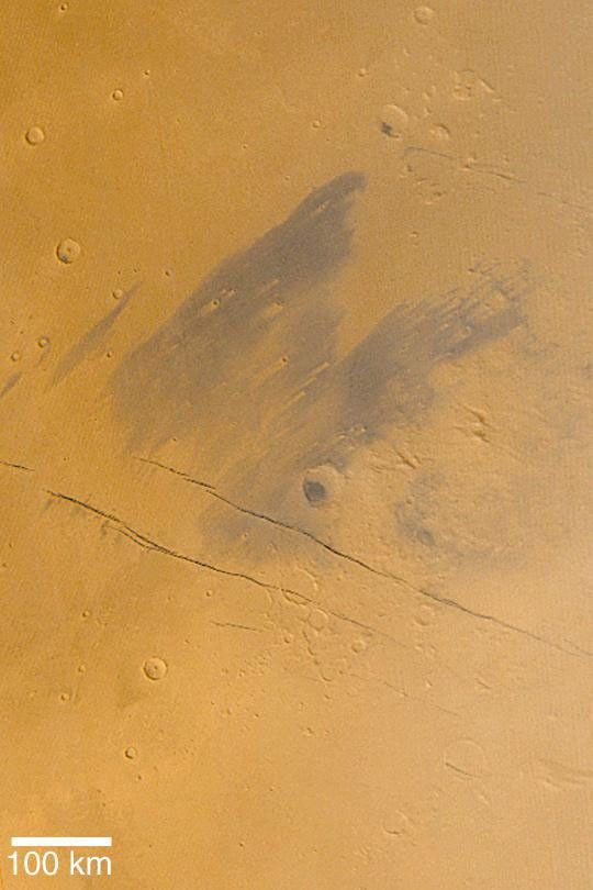 NASA's Mars Global Surveyor shows dark, wind-streaked plains of eastern Cerberus, located southeast of the Elysium volcanoes. The dark, diagonal lines are the Cerberus Fossae, a series of cracks where the surface of Mars has literally split open.