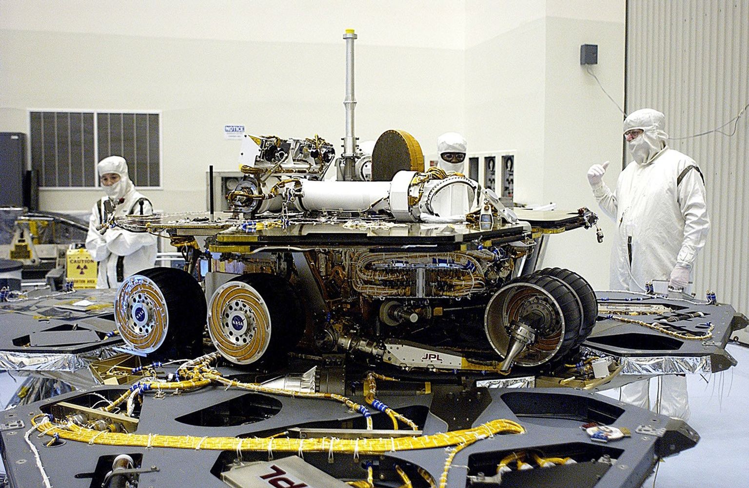 In the Payload Hazardous Servicing Facility, the lander petals of the Mars Exploration Rover 2 (MER-2) have been reopened and its solar panels deployed to allow technicians access to the spacecraft to remove one of its circuit boards.