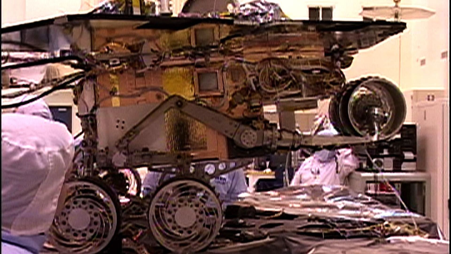 This image taken at NASA's Jet Propulsion Laboratory shows engineers testing the rover stand-up motions. The rover is in an elevated pose, preparing to fold down its wheels, descend and stand up.