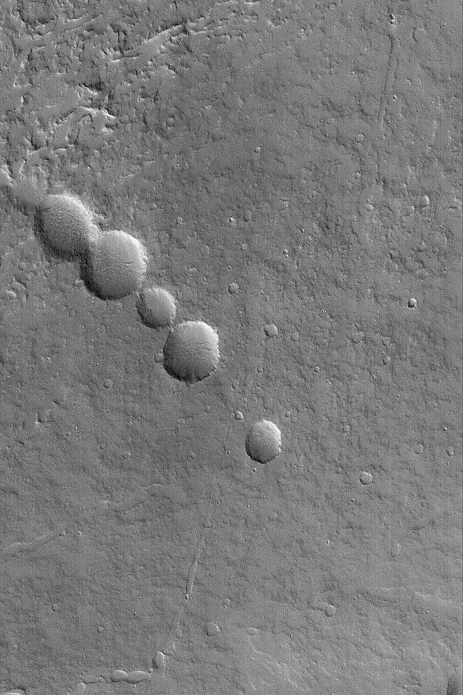 NASA's Mars Global Surveyor shows a chain of collapse pits on the lower northeast flank of the large martian volcano, Olympus Mons.