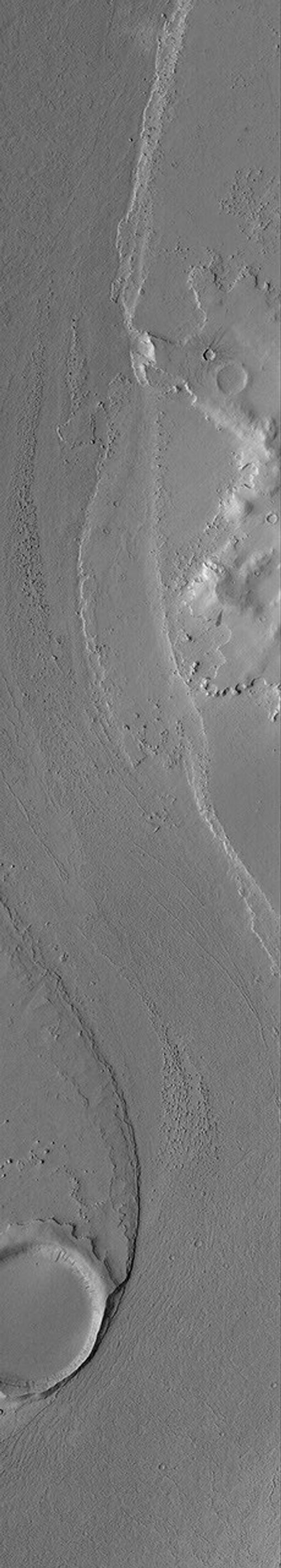 NASA's Mars Global Surveyor shows a portion of a channel in the Marte Valles outflow system on Mars. An old meteor impact crater blocked the erosive fluids that poured through Marte Vallis, creating a streamlined tail in its lee.