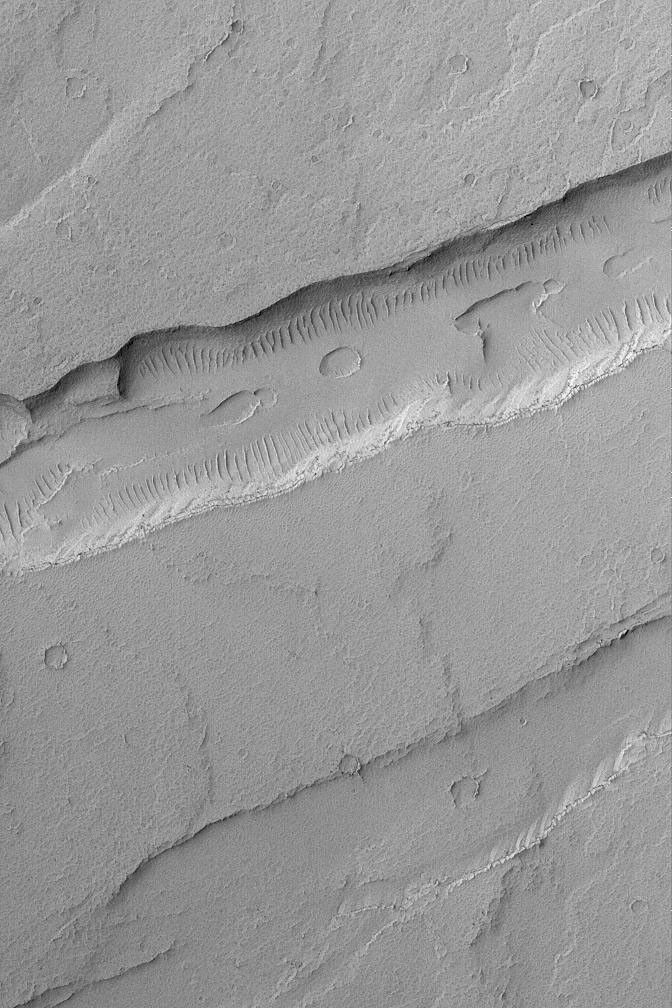 NASA's Mars Global Surveyor shows troughs and a pit chain (on the floor of the deeper trough) located immediately northeast of the giant Tharsis volcano, Arsia Mons on Mars.
