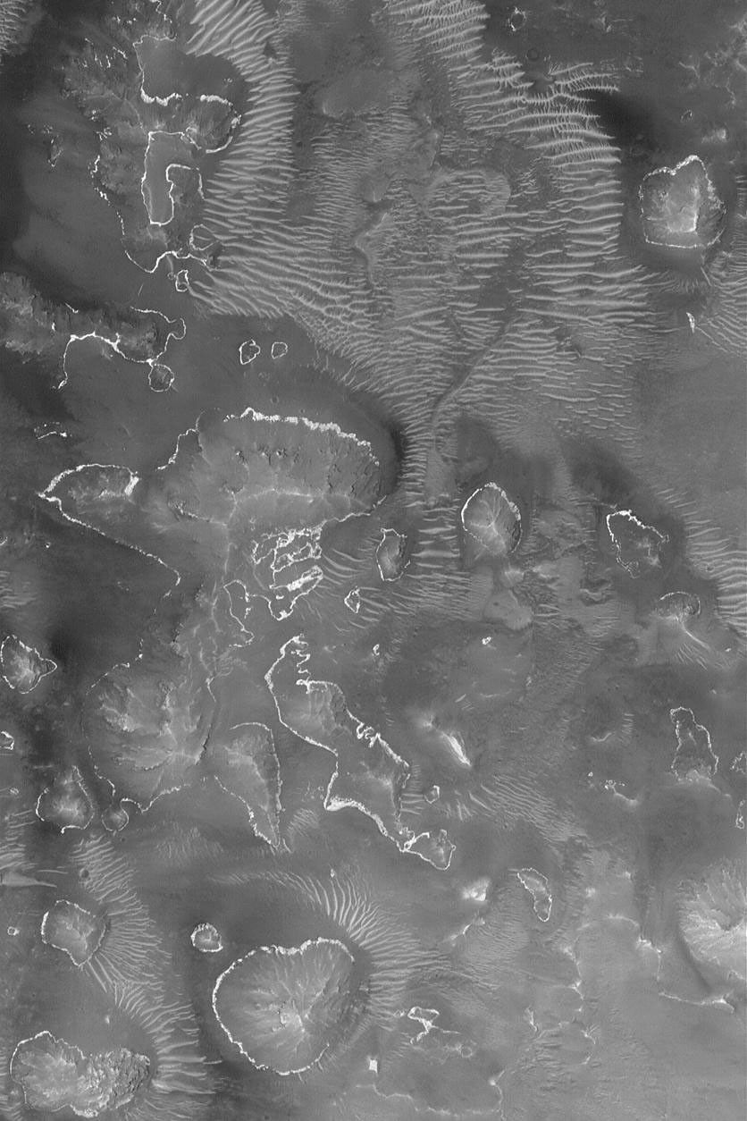 NASA's Mars Global Surveyor shows outcroppings of a light-toned rock layer on the lower slopes of buttes, hills, and massifs within one of the depressions of the Labyrinthus Noctis (Labyrinth of Night) system of the western Valles Marineris.