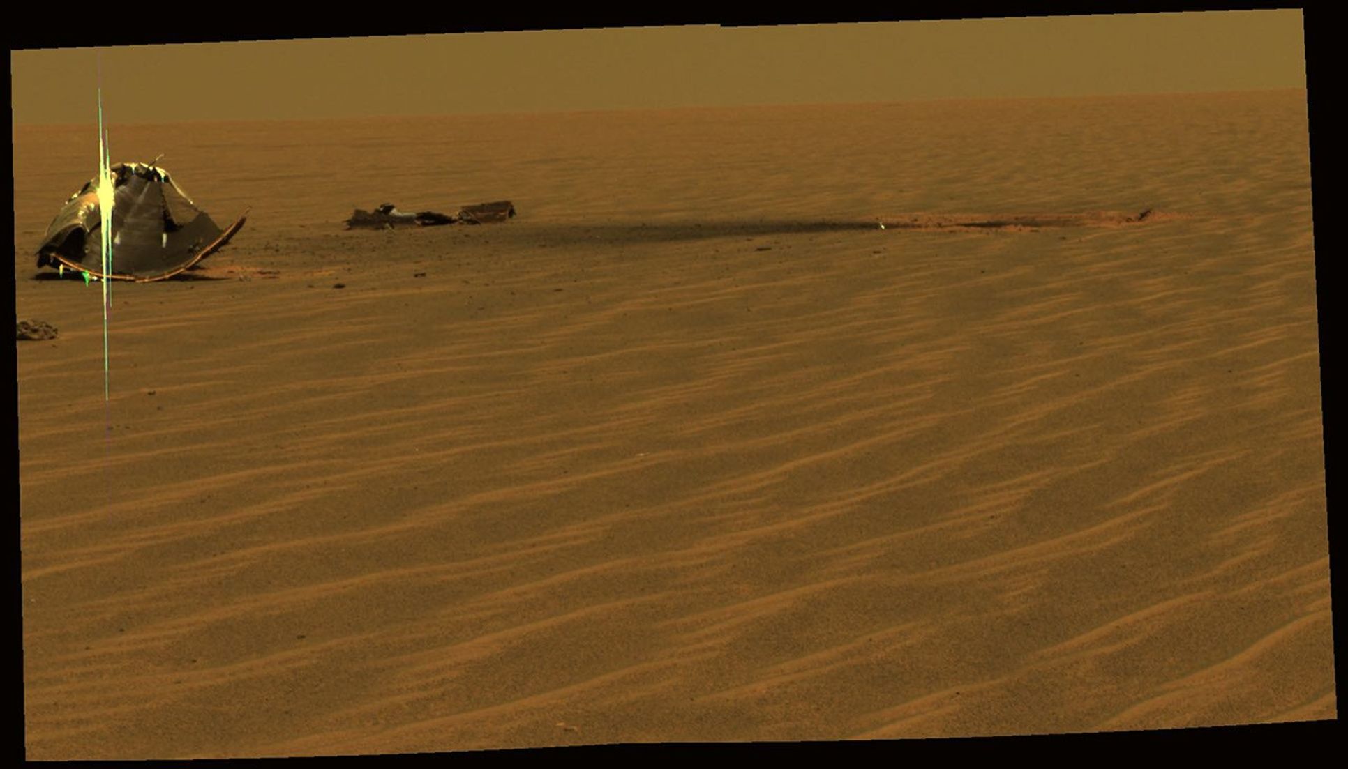 This image from NASA's Mars Exploration Rover Opportunity shows the remains of its heat shield, broken into two key pieces, the main piece on the left side and a broken-off flank piece. The heat shield impact site is identified by the circle of red dust.