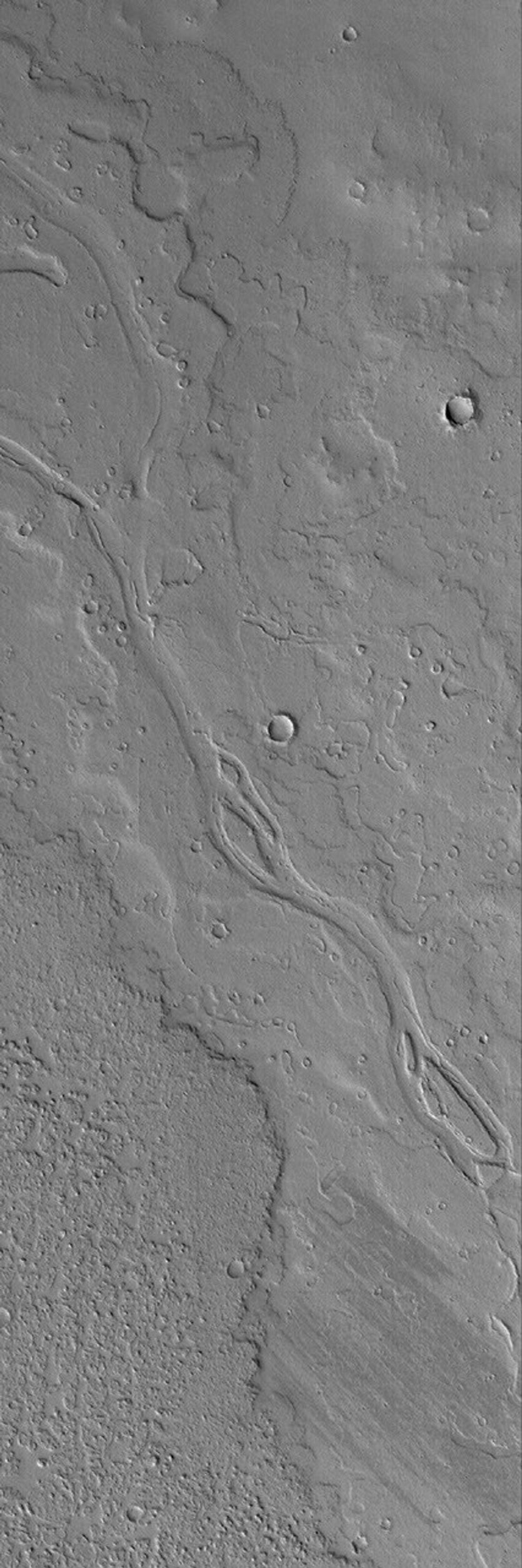 NASA's Mars Global Surveyor shows a portion of a dust-covered plain northwest of Jovis Tholus on Mars which is host to several overlapping, ancient lava flows and a channel containing streamlined features indicative of fluid flow.