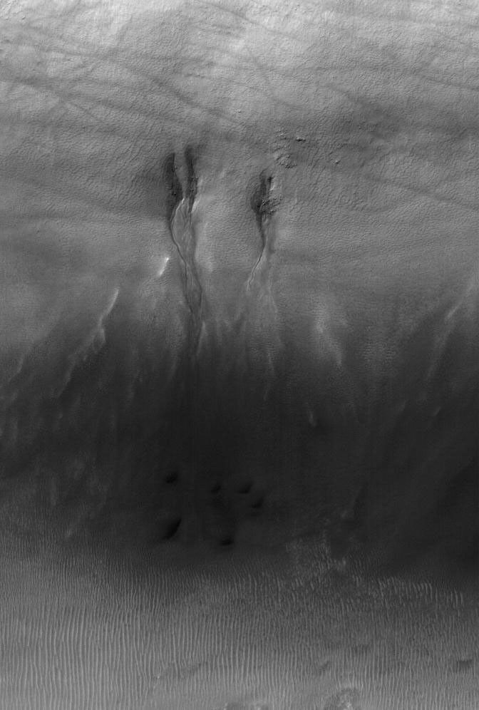 NASA's Mars Global Surveyor shows gullies in the north wall of a crater south of Proctor Crater in Noachis Terra on Mars. Dark streaks cutting across the scene were formed by passing dust devils.