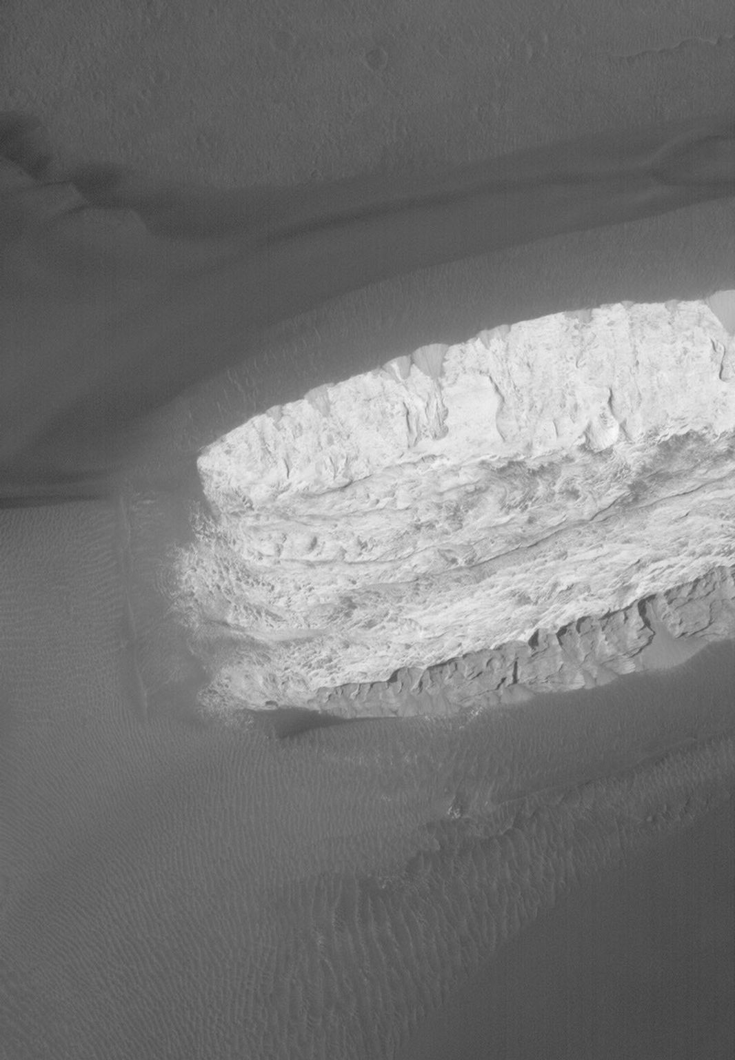 This image from NASA's Mars Global Surveyor shows dark-toned, windblown sands and ripples, surrounding a light-toned hill, interpreted to be sedimentary rock, in Ganges Chasma, part of the giant Valles Marineris trough system on Mars.