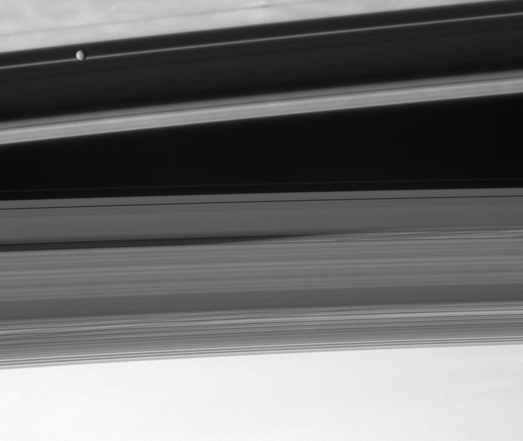 NASA's Cassini spacecraft looks upward from beneath the ringplane to spy the moon Mimas floating above the shadowed cloudtops of the Saturnian north in this image taken on Sept. 18, 2007.