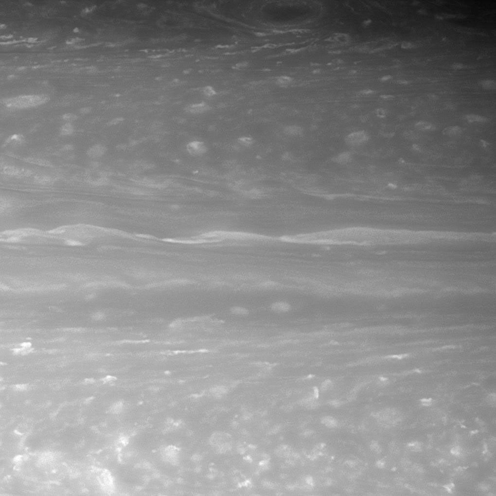 A transitional region in Saturn's atmosphere features long, linear cloud shapes, flanked to the north and south by more turbulent swirls. A dark vortex swirls ringed by bright clouds. This image was captured by NASA's Cassini spacecraft on Nov.8, 2007.