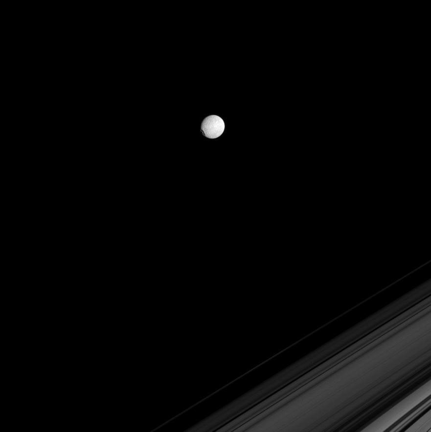 NASA's Cassini spacecraft spies Saturn's icy moon Mimas on the far side of Saturn's rings. The large crater Herschel gives the moon a flattened profile on its leading hemisphere, at left.