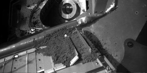 The Robotic Arm of NASA's Phoenix Mars Lander released a sample of Martian soil onto a screened opening of the lander's Thermal and Evolved-Gas Analyzer (TEGA) during the 12th Martian day, or sol, since landing (June 6, 2008).