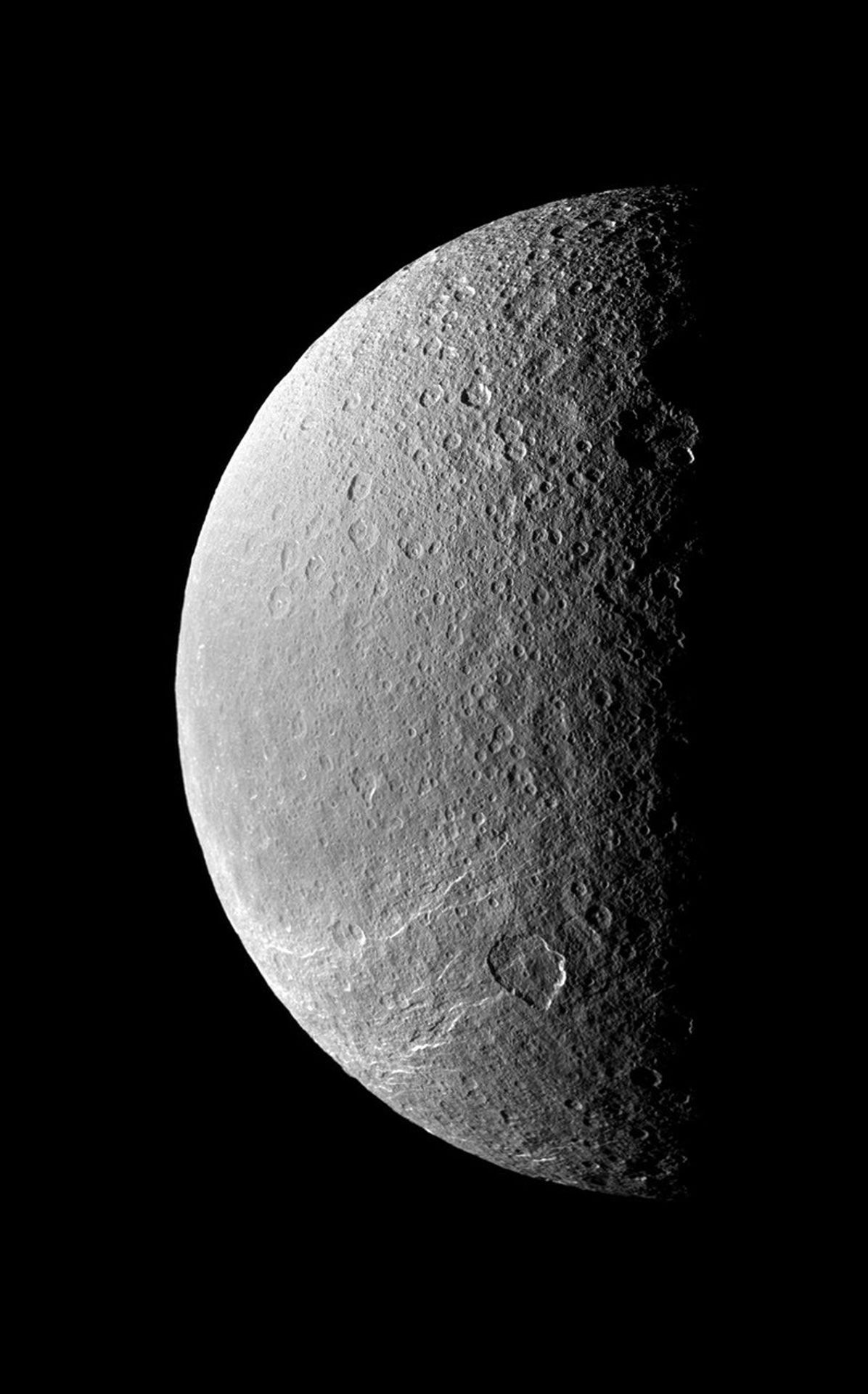 The terminator between light and dark throws Rhea's cratered surface into stark relief while the southern hemisphere is scored by bright icy cliffs. This image was taken in visible light with NASA's Cassini spacecraft's narrow-angle camera.