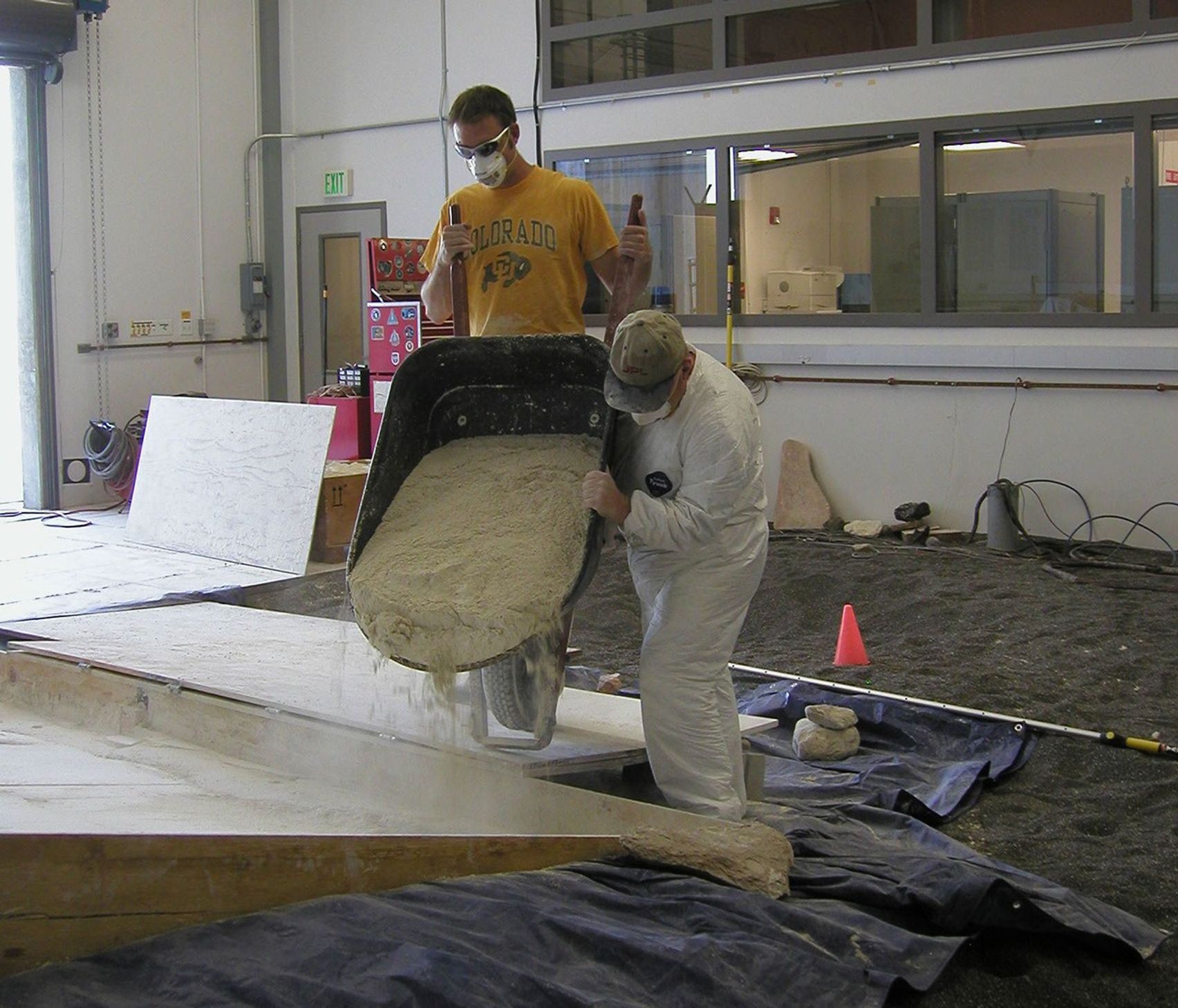 Rover team members Mike Seibert (left) and Paolo Bellutta add a barrowful of soil mixture to the sloped box where a test rover will be used for assessing possible maneuvers for NASA's rover Spirit to use in escaping from a sandtrap on Mars.
